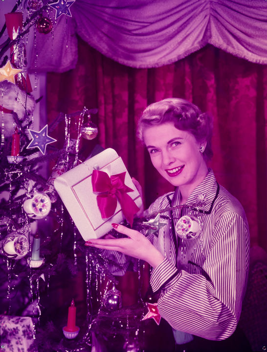 Glamorous woman holds present beside Christmas tree, c.1950, Photographic Advertising Limited © National Media Museum, Bradford / SSPL. Creative Commons BY-NC-SA