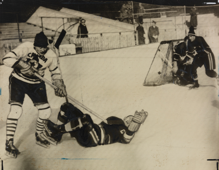 An ice hockey player striking another player on the ground with his stick