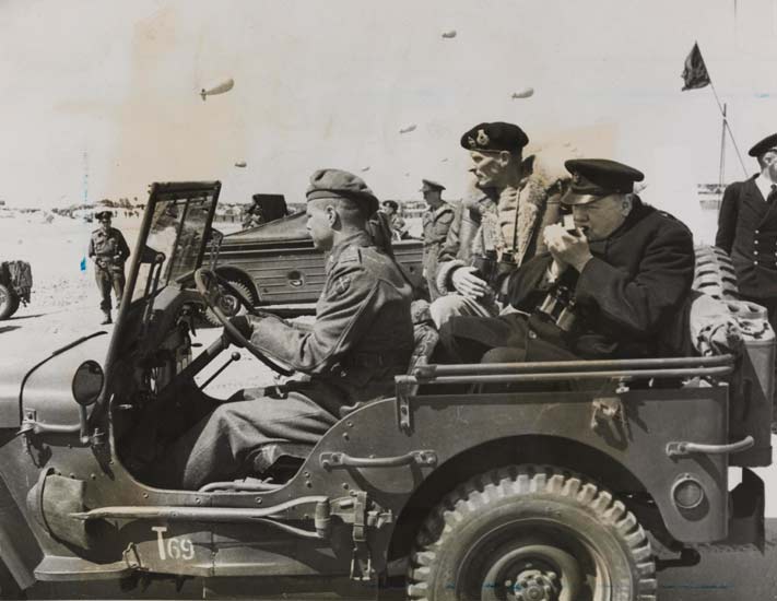Churchill in the back of a Jeep lighting a cigar, in Normandy just after D-Day