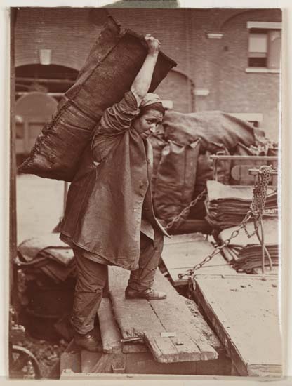 Black and white picture of a woman carrying a sack of coal on her back