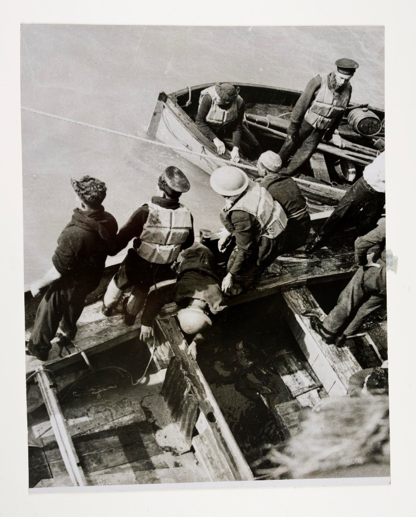 A photograph of a solider being helped onto a board at Dunkirk