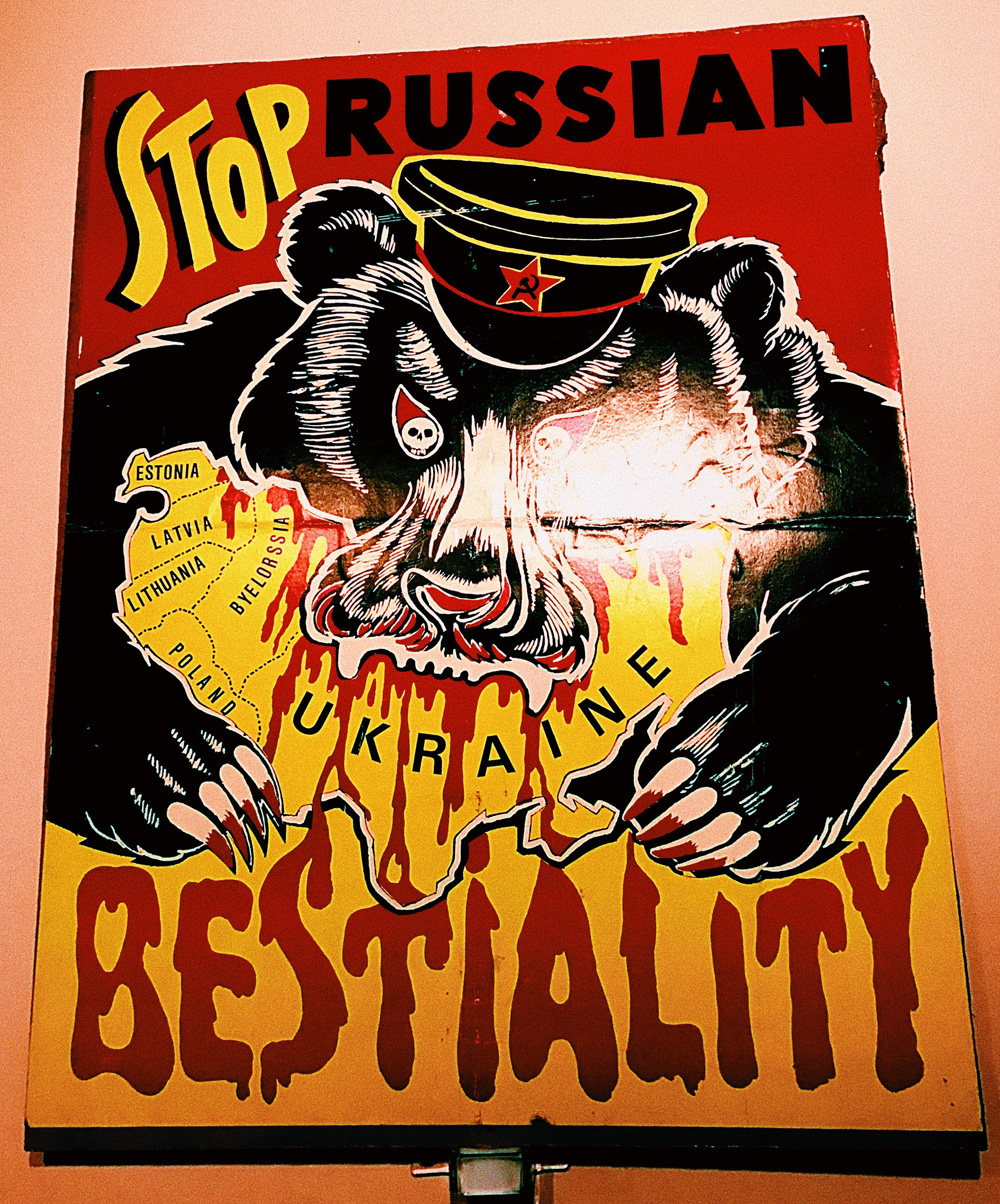 Illustrated placard with image of Russian bear biting into Ukraine and the words 'Stop Russian Bestiality'
