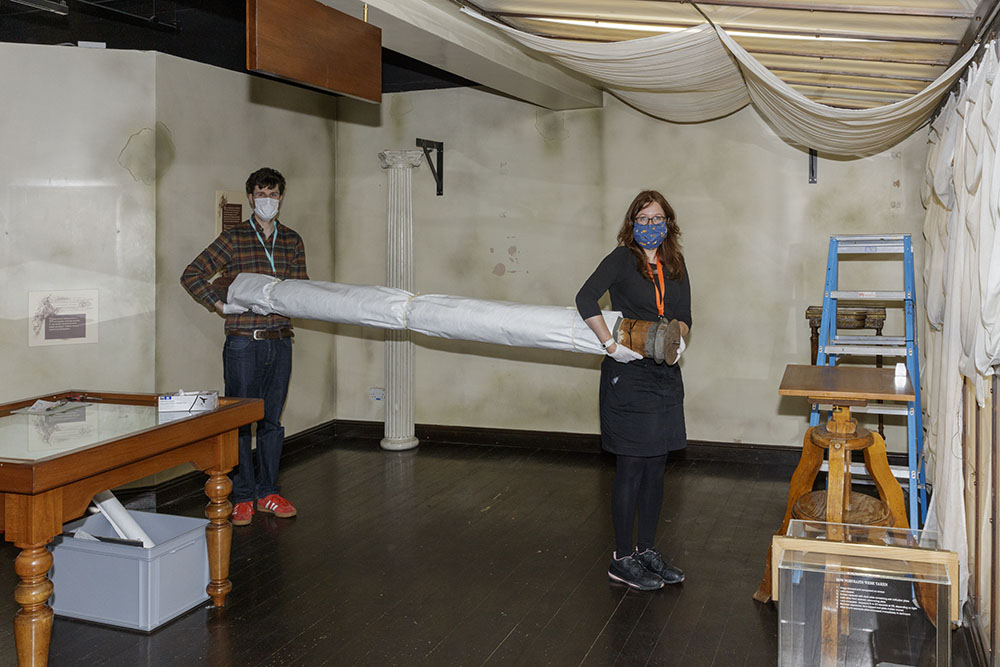 Museum staff carrying rolled-up backdrop