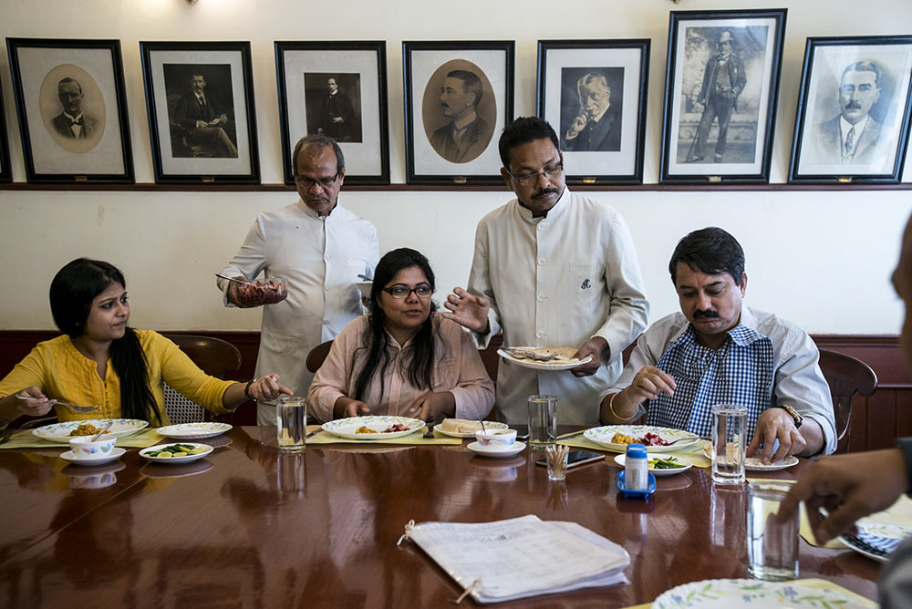 A group of people eating at a table with old portraits in the background