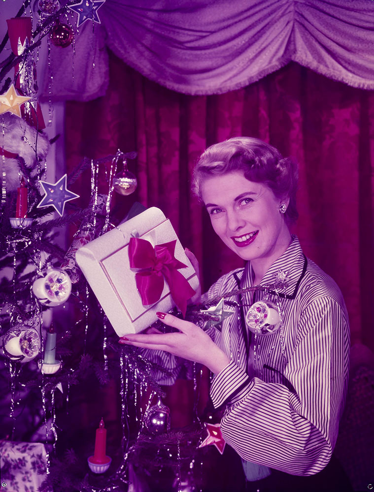 Woman holding present beside Christmas tree