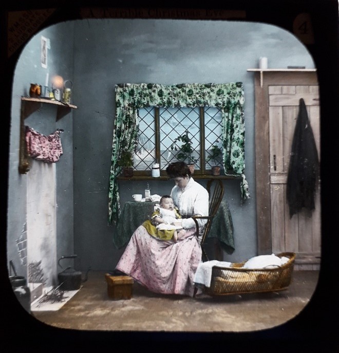 Lantern slide showing a woman, sitting in a rocking chair, holding a baby