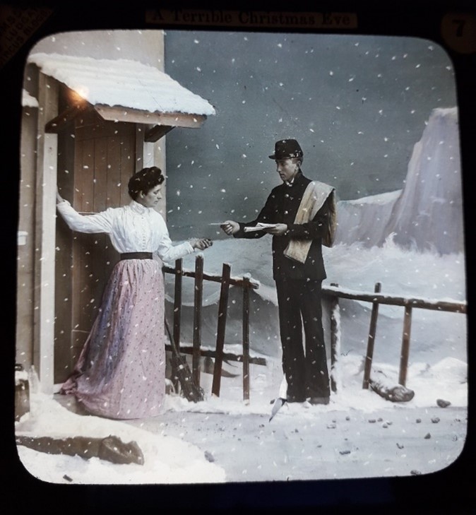 Lantern slide showing postman offering letter to woman at the door of her home; it is snowing and a stormy sea is visible in the background