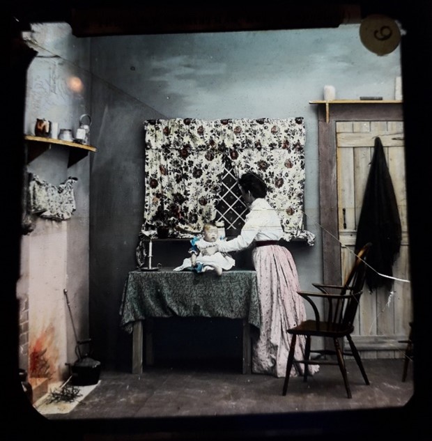 Lantern slide showing woman looking out of the window as she rests her baby on a table