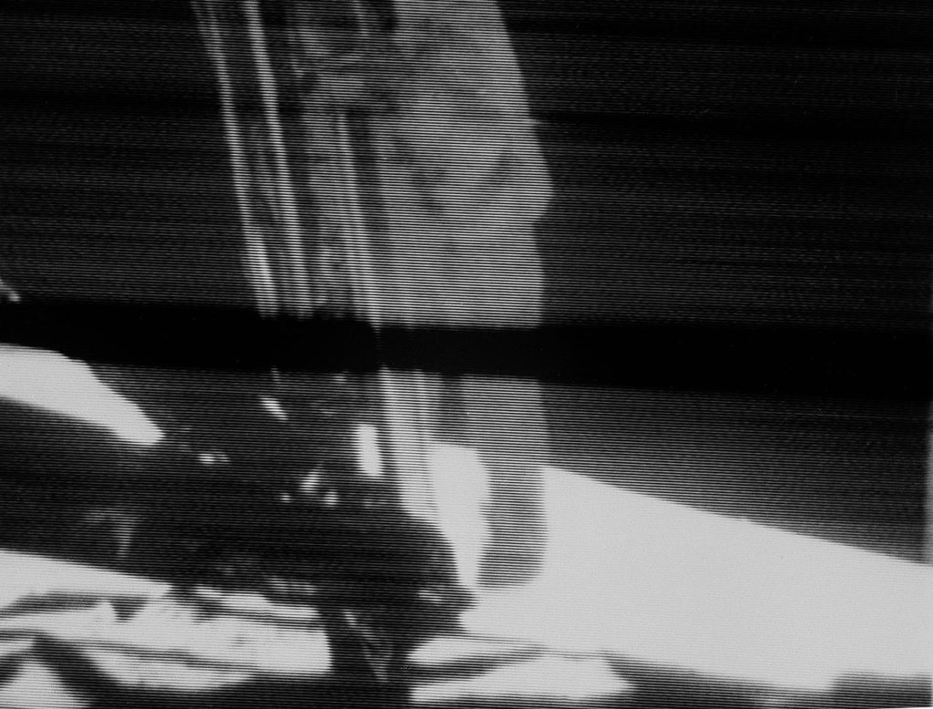Grainy image of a man in a spacesuit stepping down onto the Moon