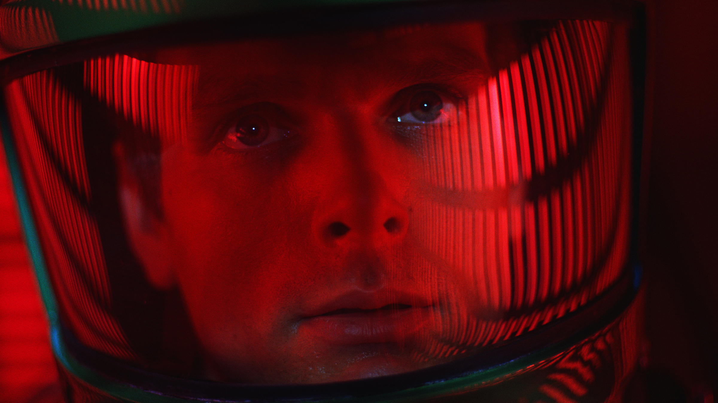 Close-up of a man's face through his space helmet, soaked in red light