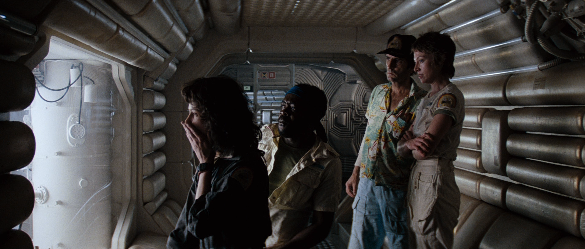 Four casually-dressed crew peer into a room on a space ship, looking shocked and apprehensive