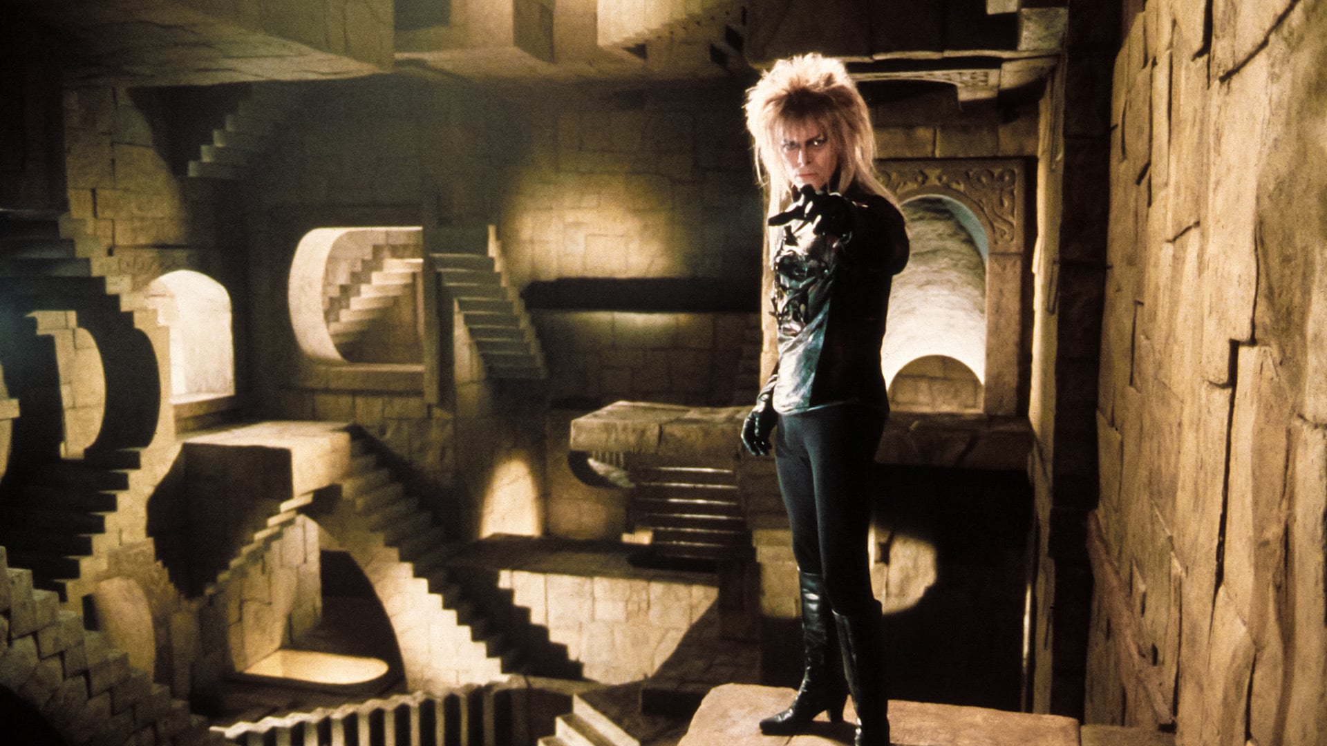 David Bowie stands in a stone labyrinth wears black leggings, blouse and gloves