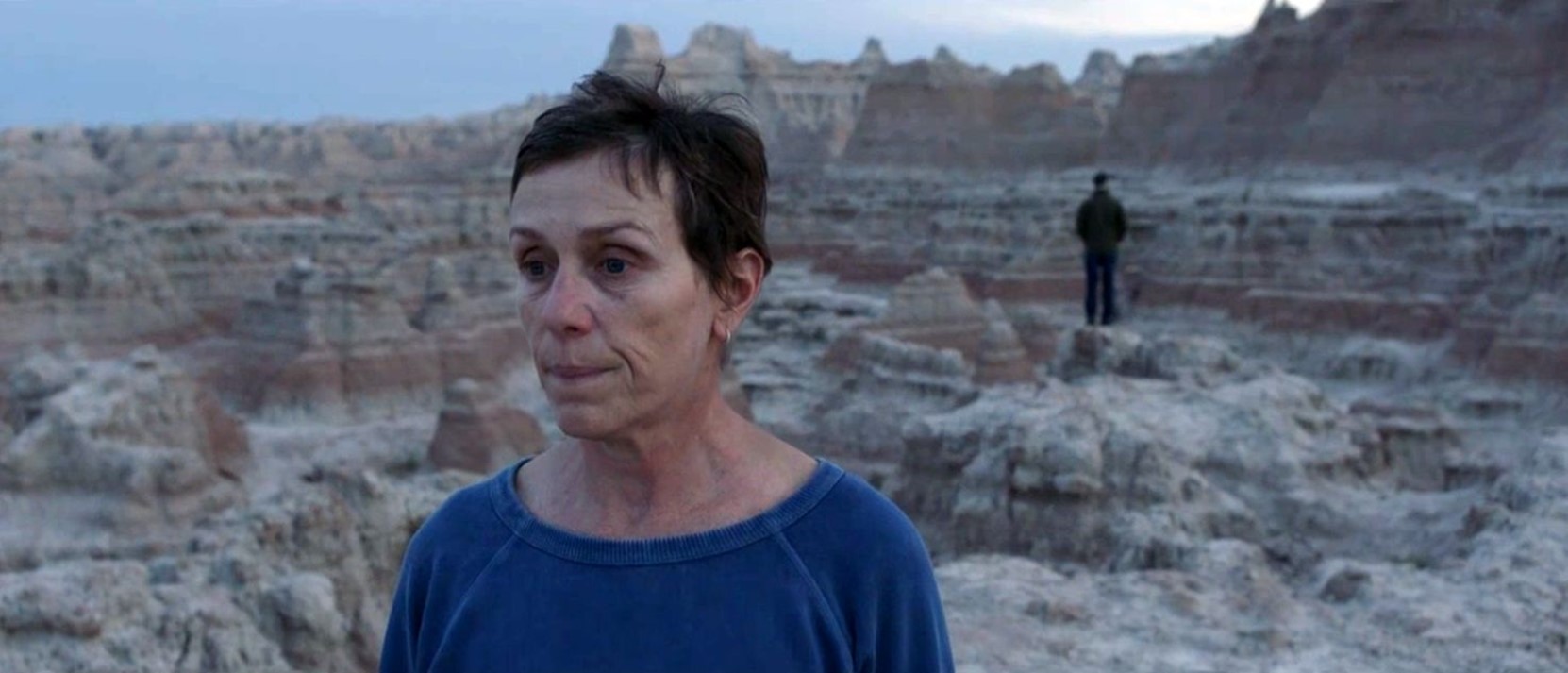 Frances McDormand stands in a rocky landscape in the southwestern USA, looking pensive