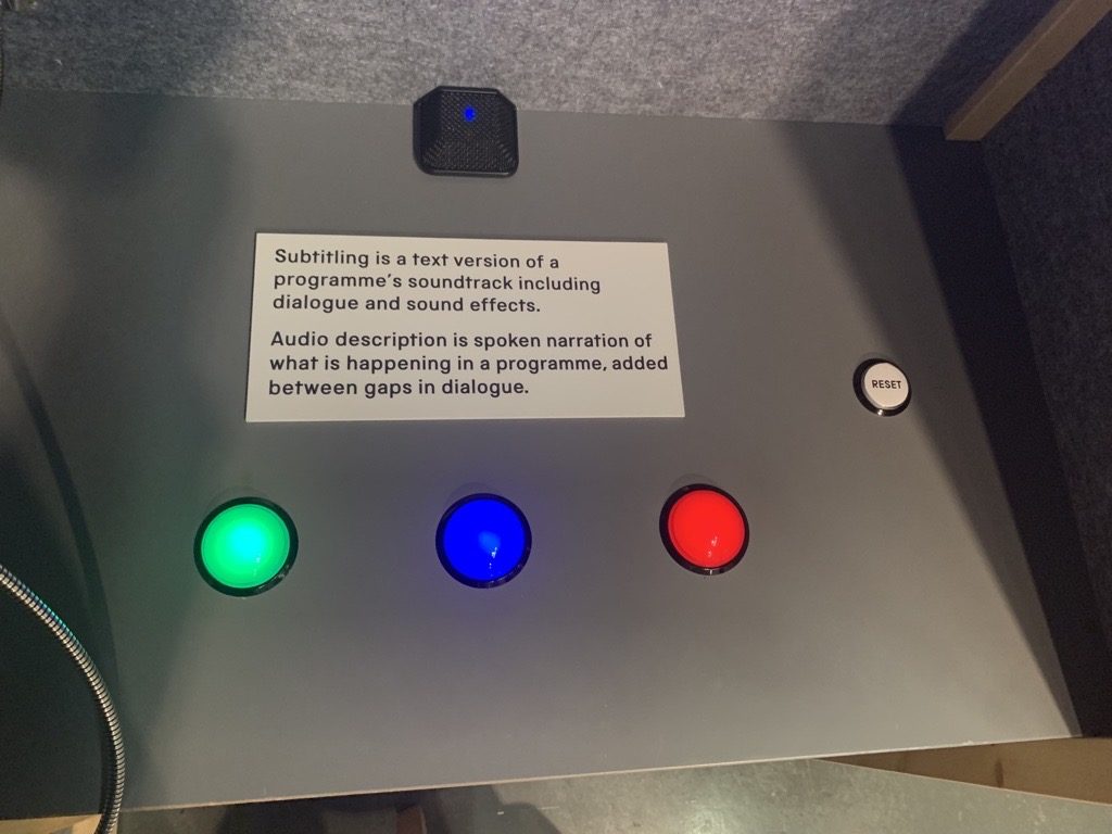 A grey desk with green, blue and red buttons and a text panel about subtitling 