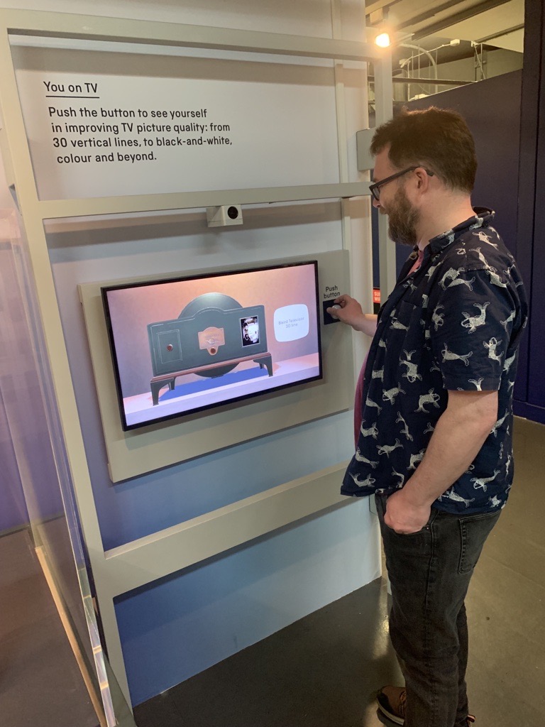 White man with a beard and glasses presses a button to operate an interactive exhibit.