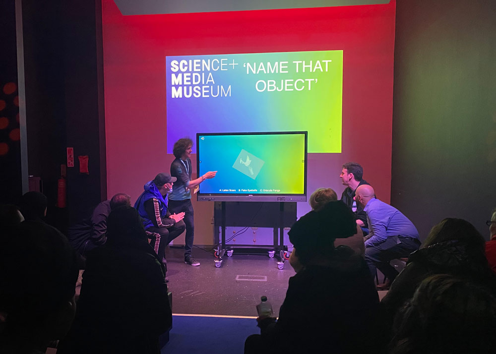 Museum staff present an interactive quiz in front of a seated audience