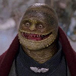 A Goomba character from a live-action film with a scaly head, staring eyes and wide mouth with pointy teeth