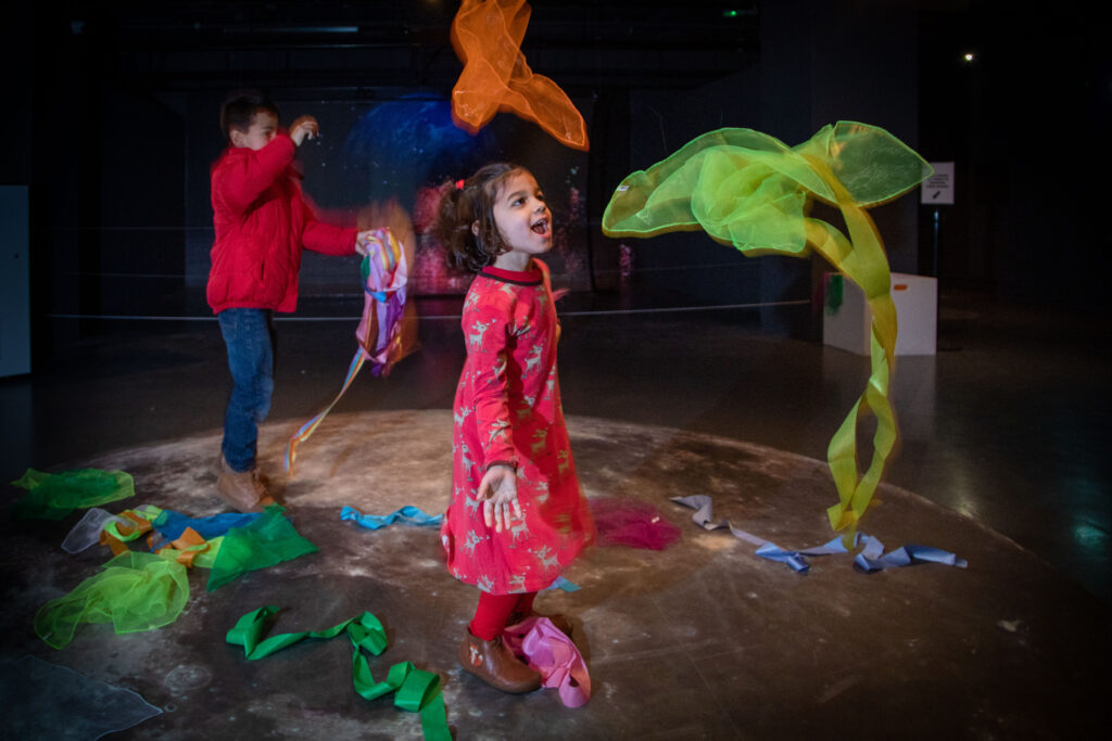 Children playing with colourful fabric strips in a dark space