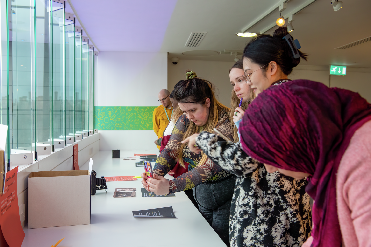 A group of people look at designs for museum displays, with some making notes or taking photos