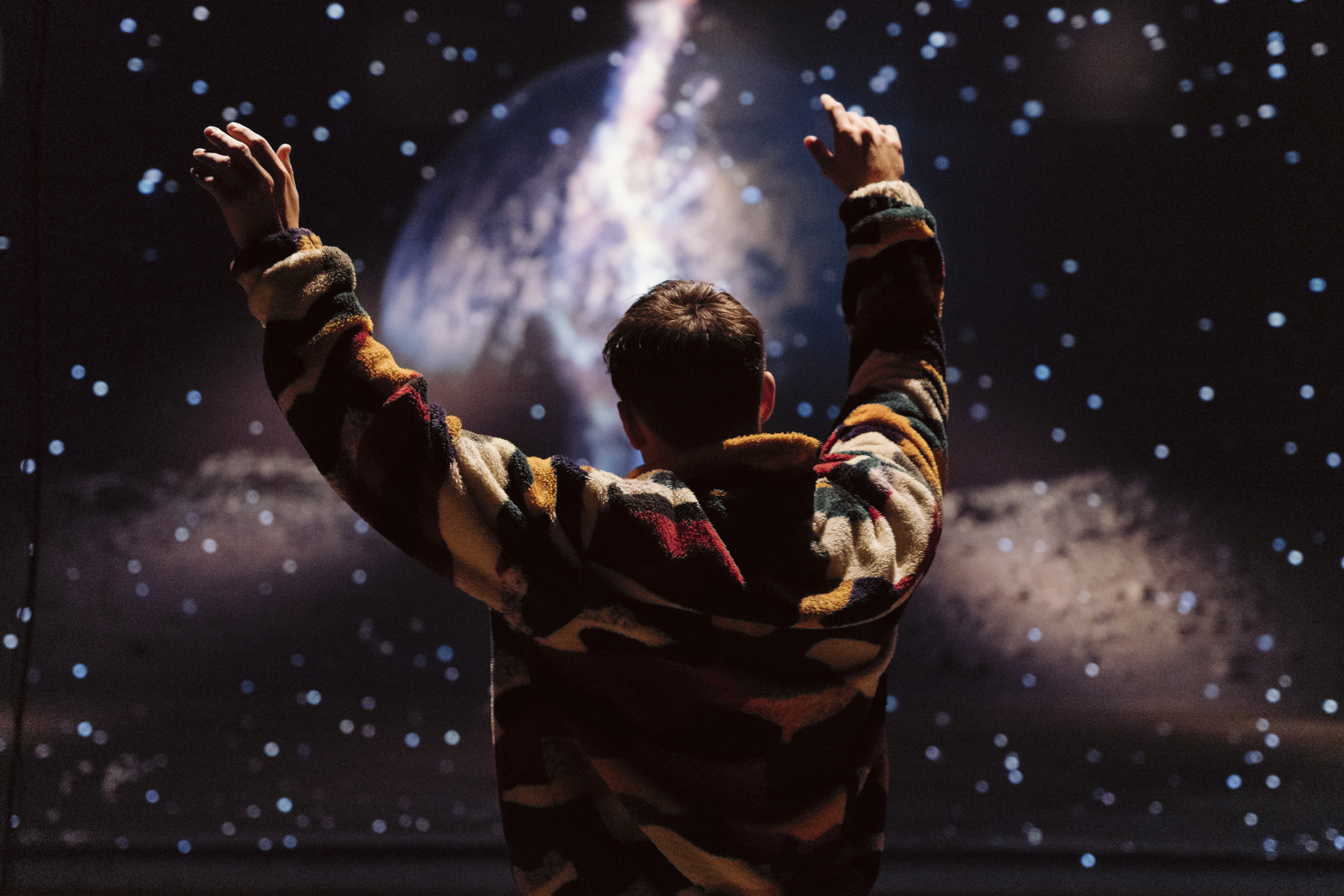 A child seen from behind raising their hands, looking at a galaxy projection