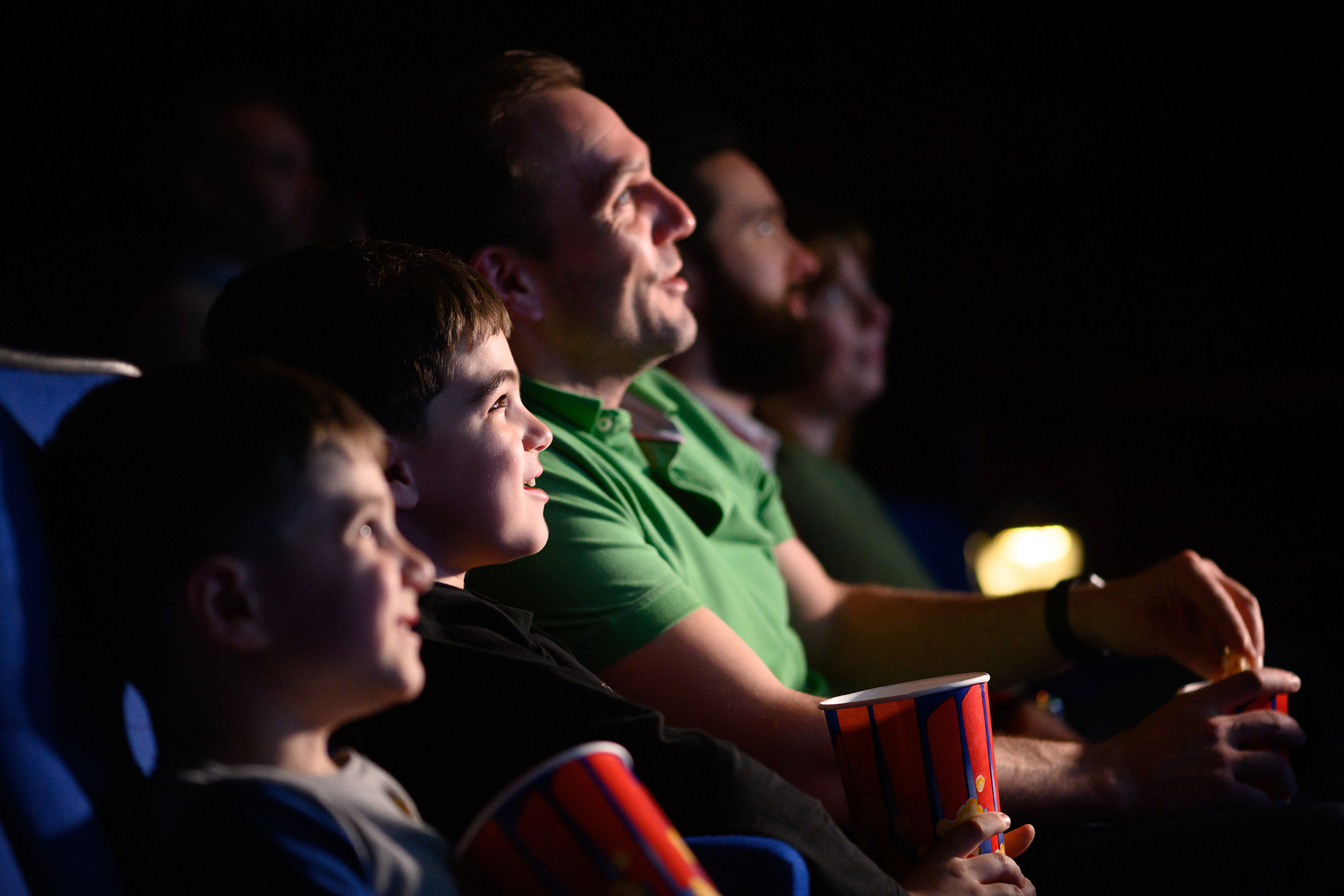 A group of children and adults watching a film, their happy faces illuminated by the screen