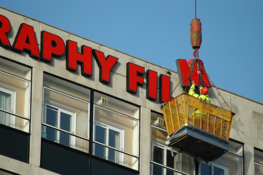 Workmen removing large name lettering from the side of a building