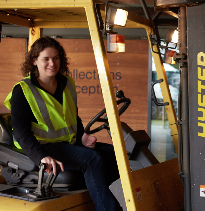 Gabby, a white woman wearing a hi-vis jacket, drives a forklift at the collections centre