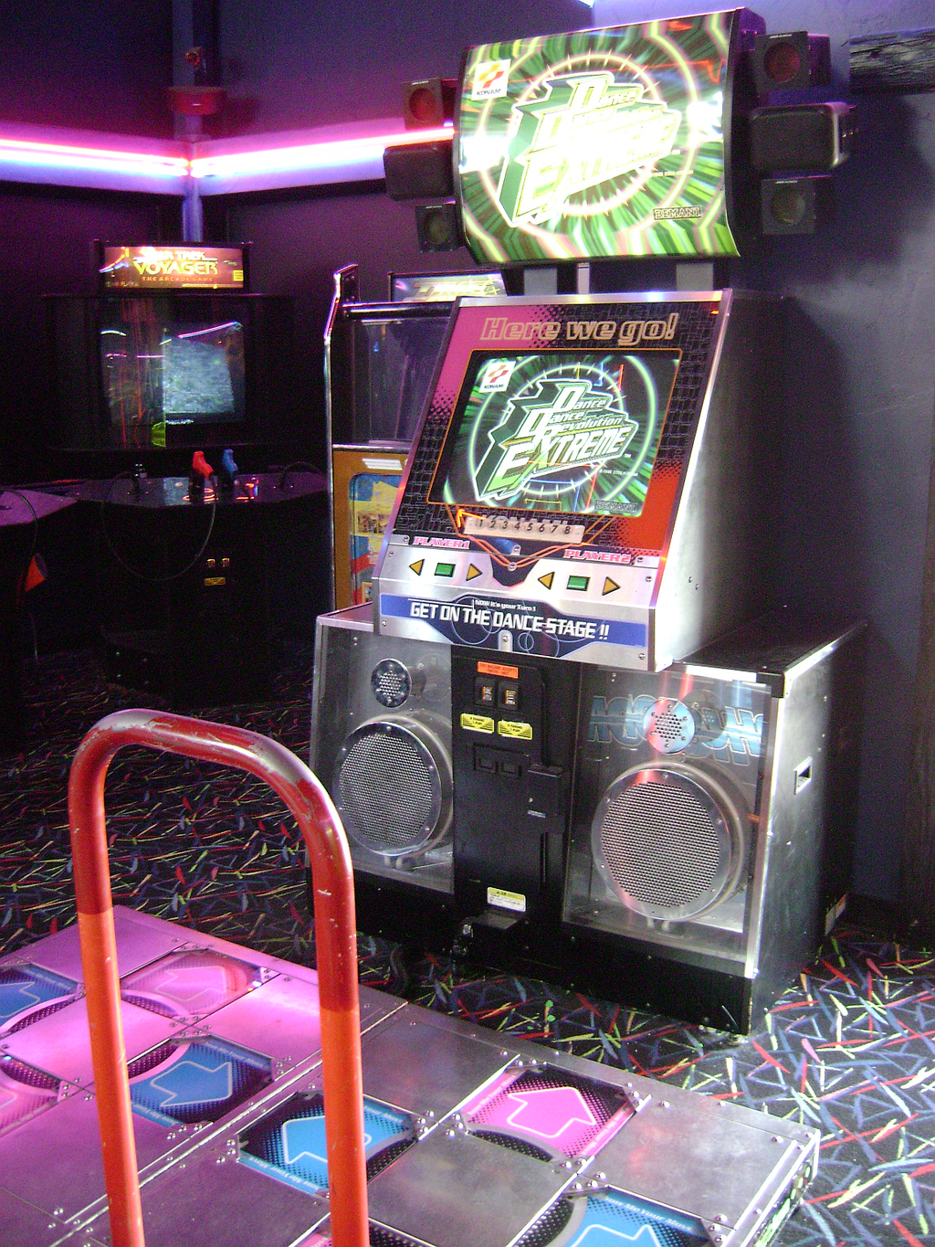 A Dance Dance Revolution game in an arcade with dark walls and a bright 80s-pattern carpet