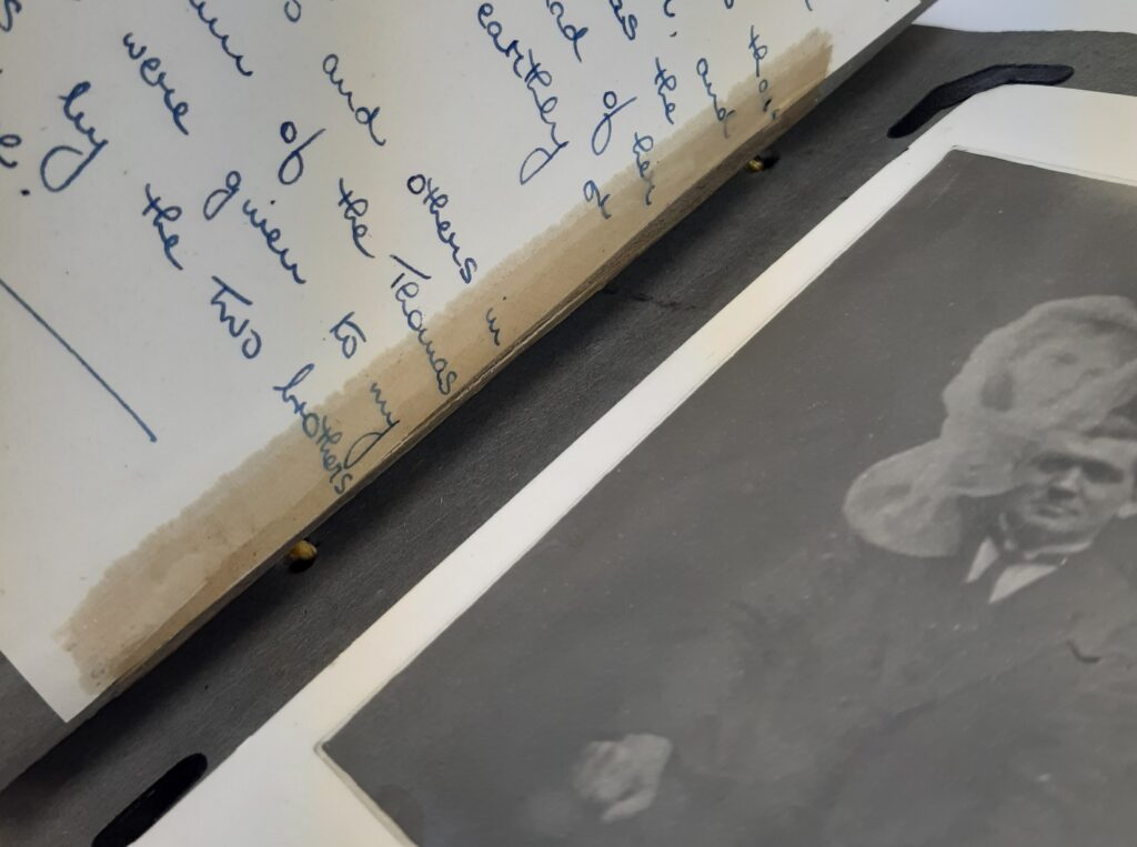 An open photograph album, showing sticky tape partially covering a page of handwriting