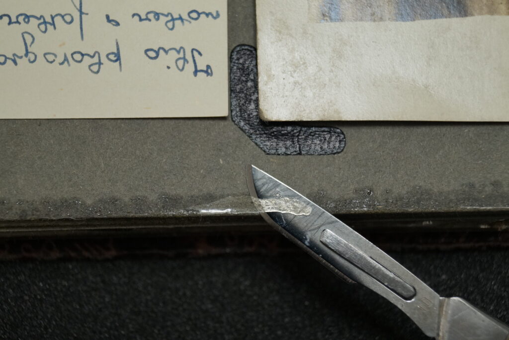 A scalpel blade removing loose tape from the edge of an old photo album