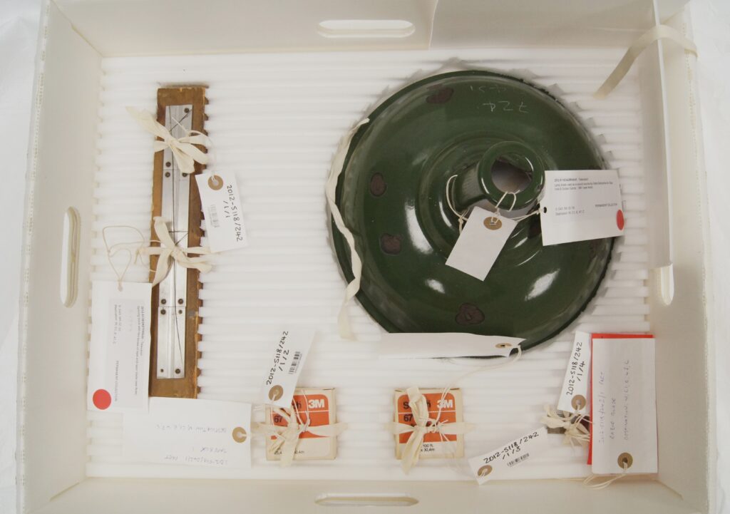 A white box filled with objects including a green metal lampshade and small boxed tape reels