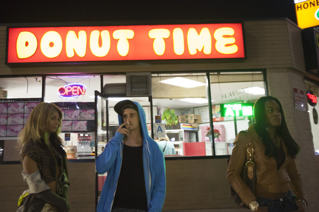 The main characters of Tangerine outside a doughnut shop with a neon sign