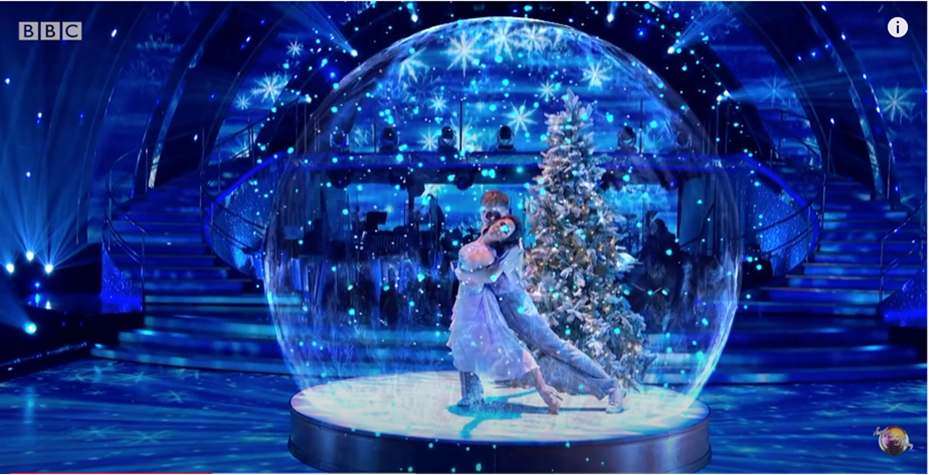 Two dancers and a Christmas tree inside a computer-generated snow globe