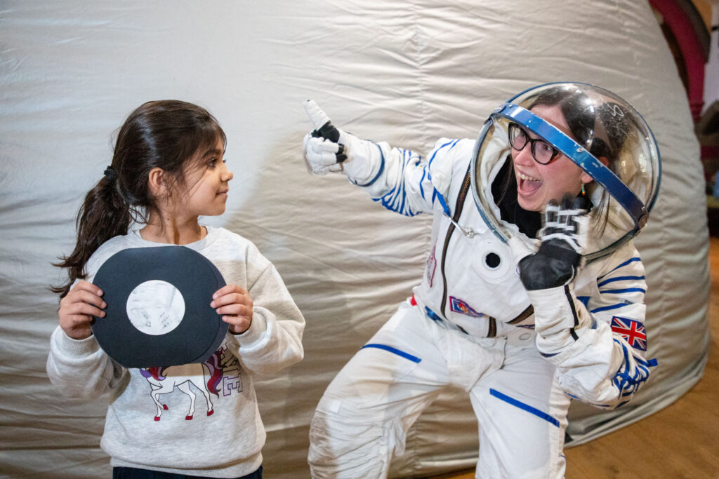 A person in an astronaut costume gives a young girl the thumbs up