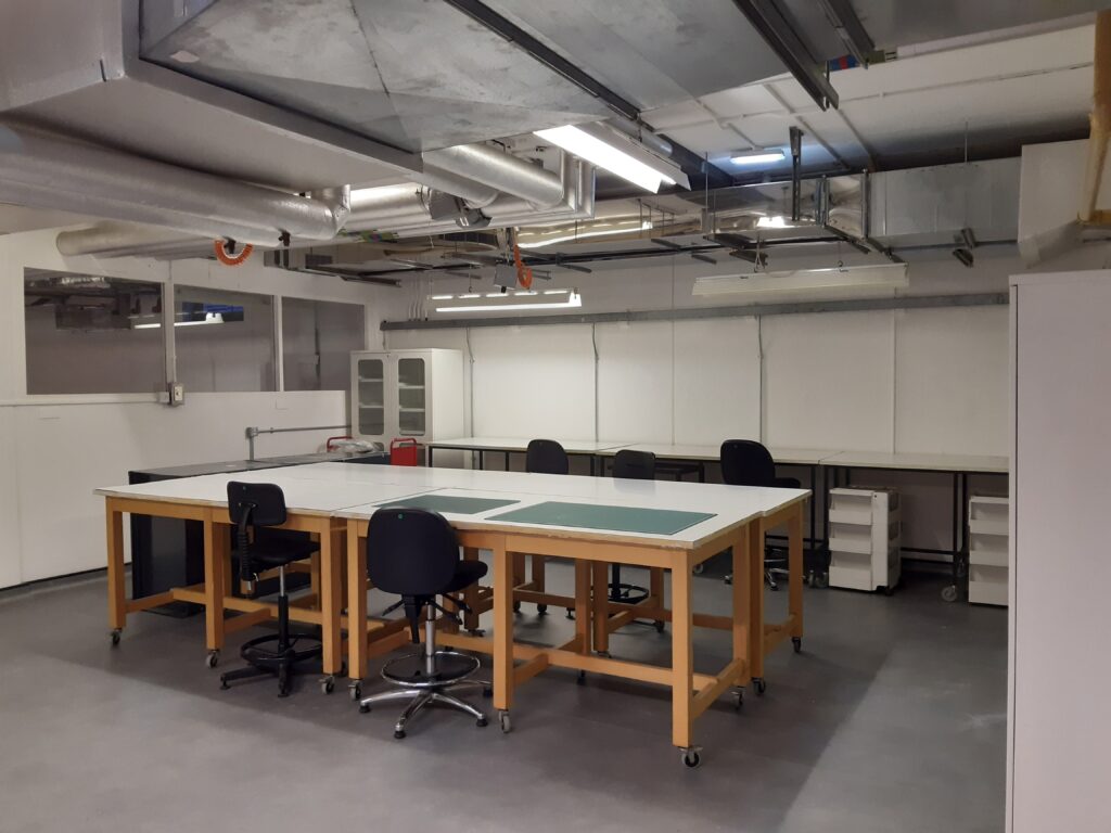A basement room with large workbench, chairs and shelving