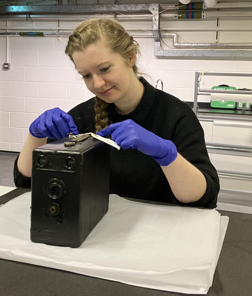 Conservator Eleanor Durrant working on a large box camera at a workbench.