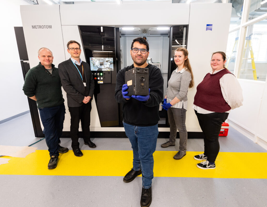 In front of the CT scanner, Curator Saquib Idrees holds up the Midg camera, watched by NSMM conservators and University of Bradford staff.