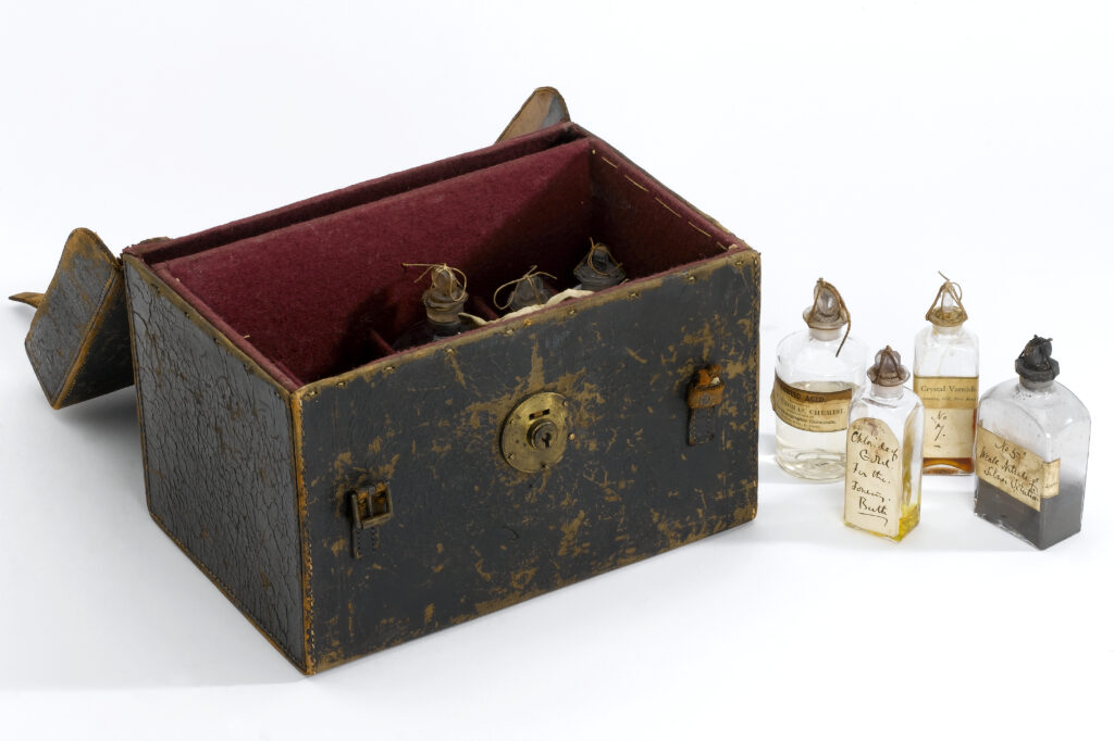 A black leather box with red lining, and several glass bottles with handwritten labels.