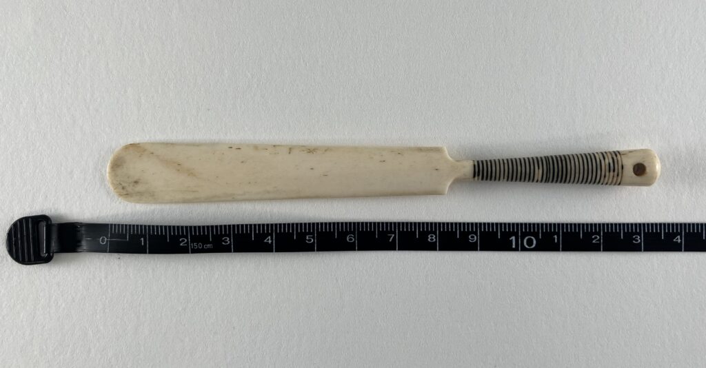 An w hite letter opener laid next to a tape measure, showing it measures 10.35 centimetres.