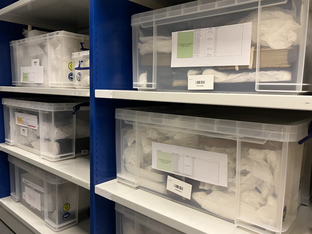 Clear plastic boxes full of tissue-wrapped objects on metal shelving.