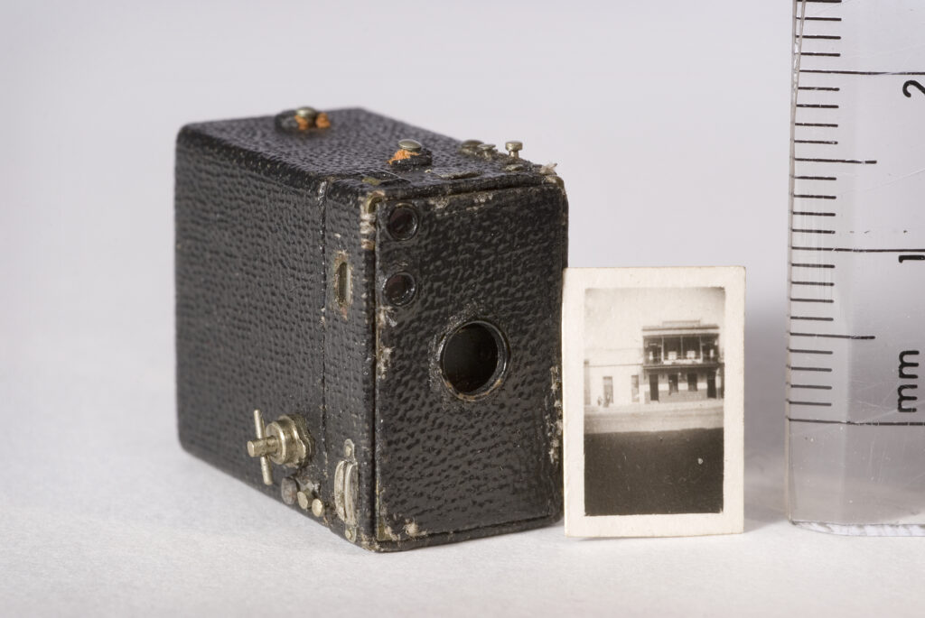 Miniature box camera and photo next to a ruler showing its size