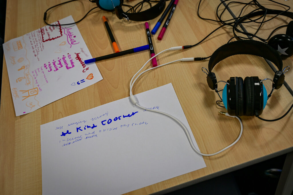 A table with headphones, pens and paper sheets with ideas jotted down