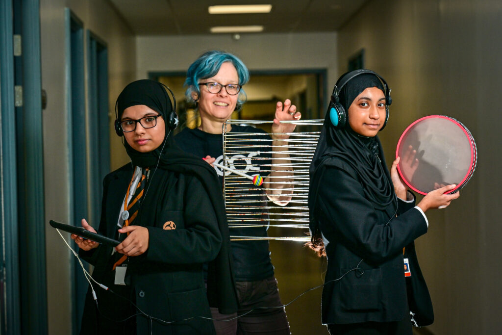 Caro C and two students holding up improvised instruments.