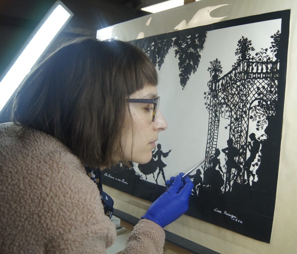 Vanessa leans close to the cut-out which is propped on an easel with a bright light facing it