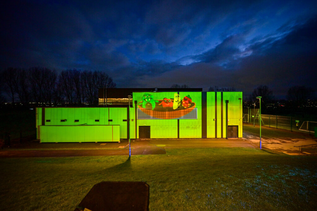 A school building lit up green with an animated film at night