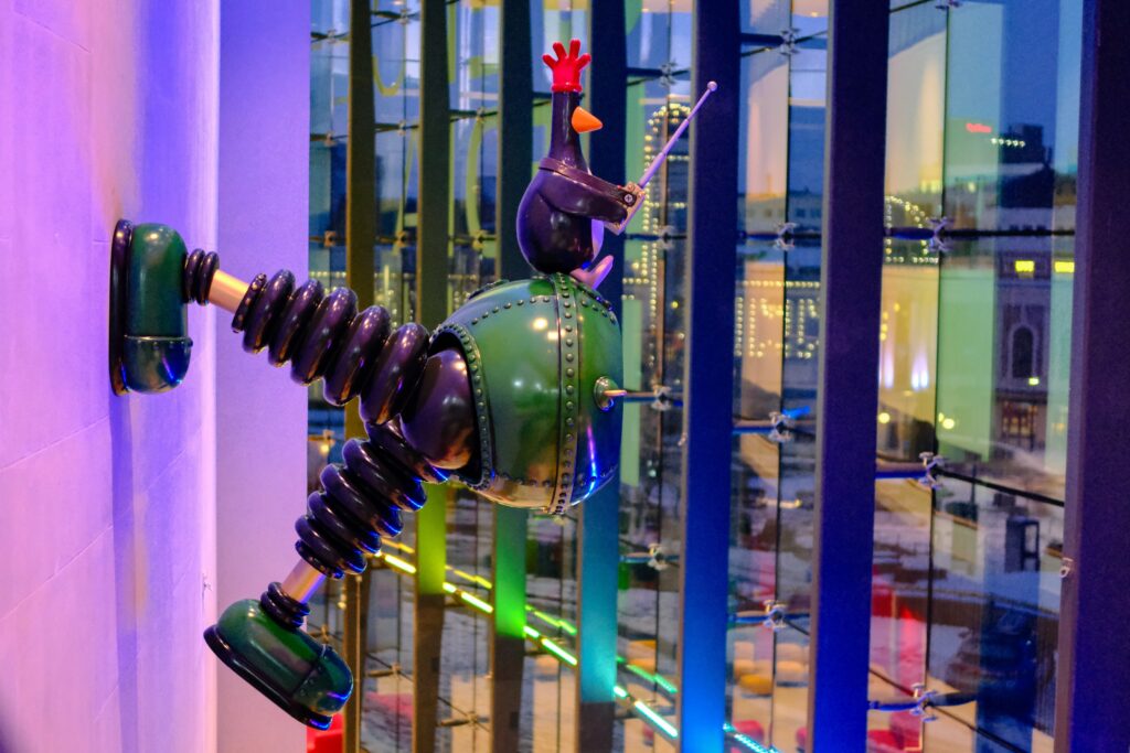 Model of mechanical trouers mounted on the wall of the museum foyer, lit with rainbow coloured lights