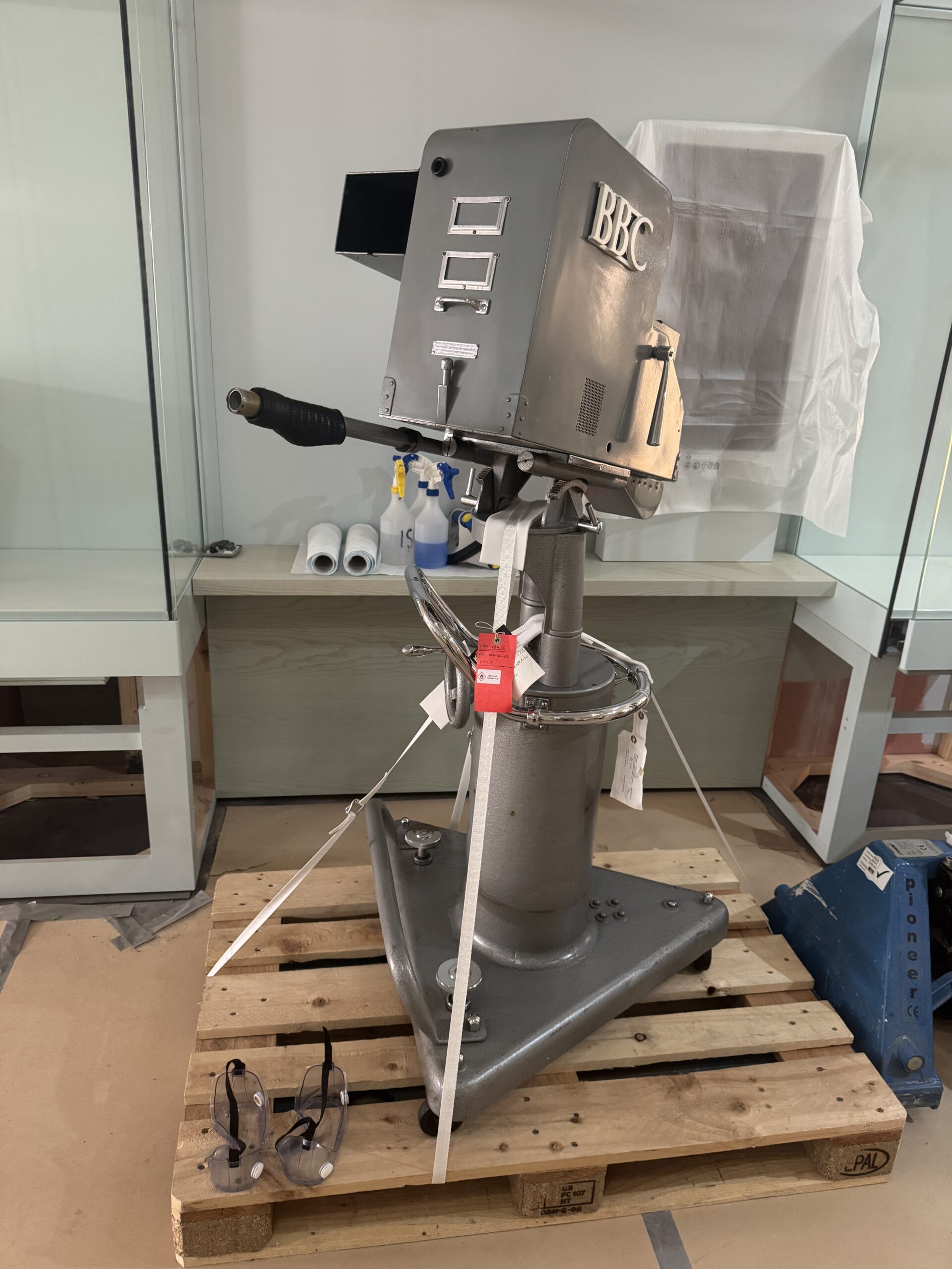 A large grey metal camera and pedestal on a wooden pallet.