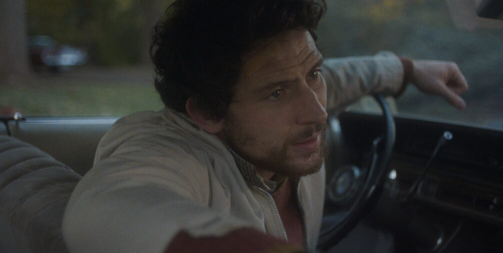 Josh O'connor sits at the wheel of a 1970s car in The Mastermind