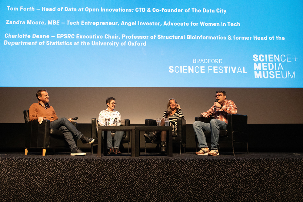 Four seated panellists on stage with the Pictureville screen just above their heads