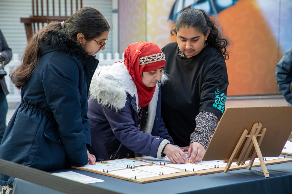 A volunteer helps two women with an activity on the table in front of them in the Broadway shopping centre.